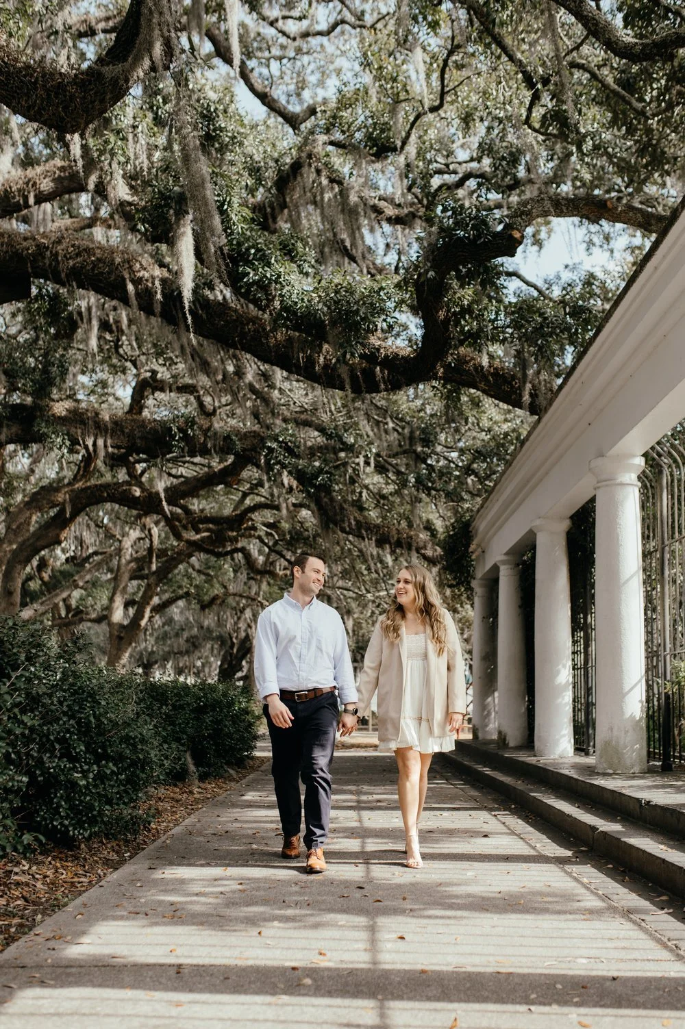 Wedding photography engagement photo by Laura Cate Photography, picturing a bride and groom couple under Spanish moss tress walking in Forsyth Park in Savannah, GA.