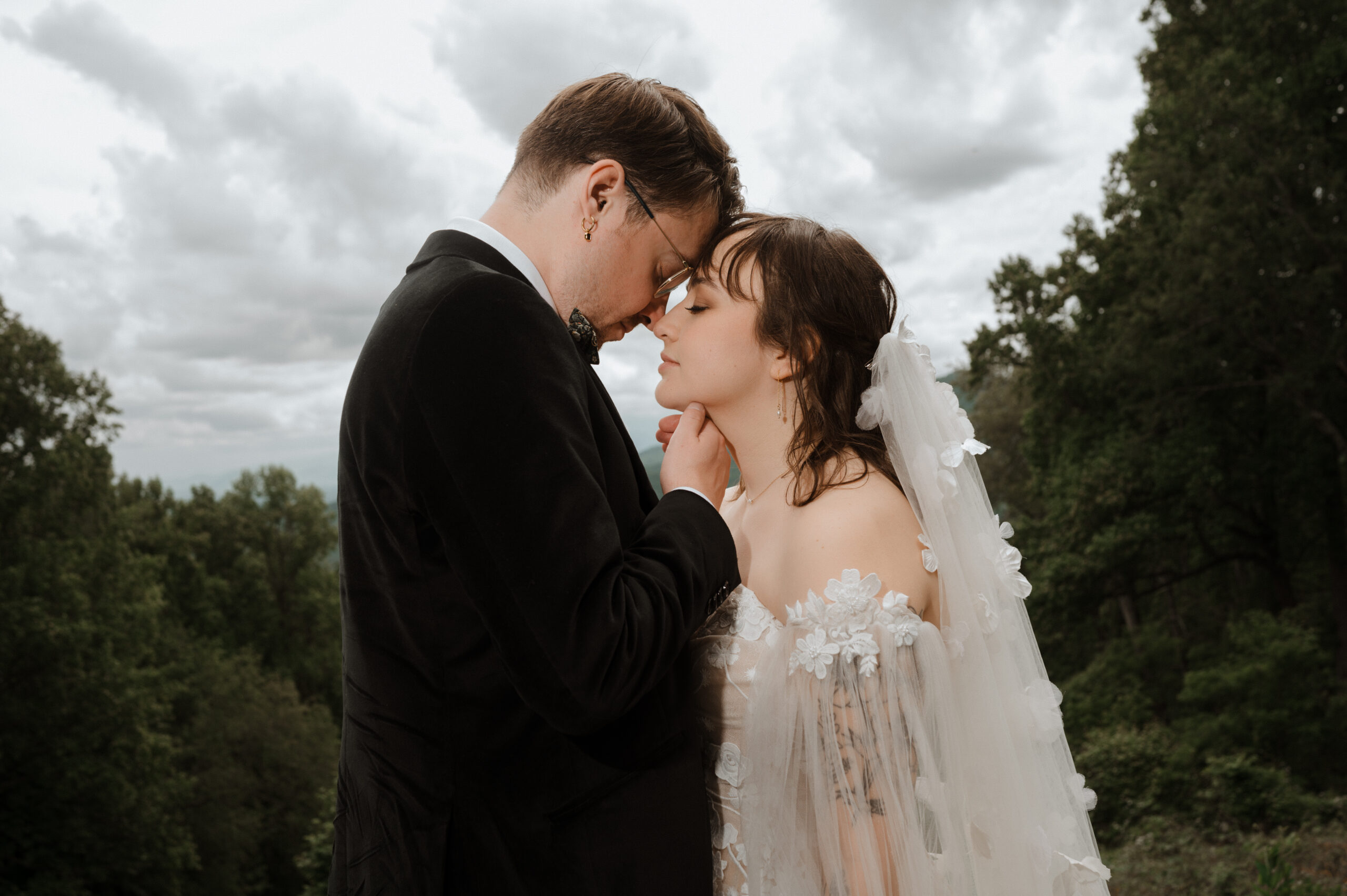 Photo by Laura Cate Photography features bride a groom couple for their wedding session photos in then Blue Ridge Mountains with a background of clouds of forest.