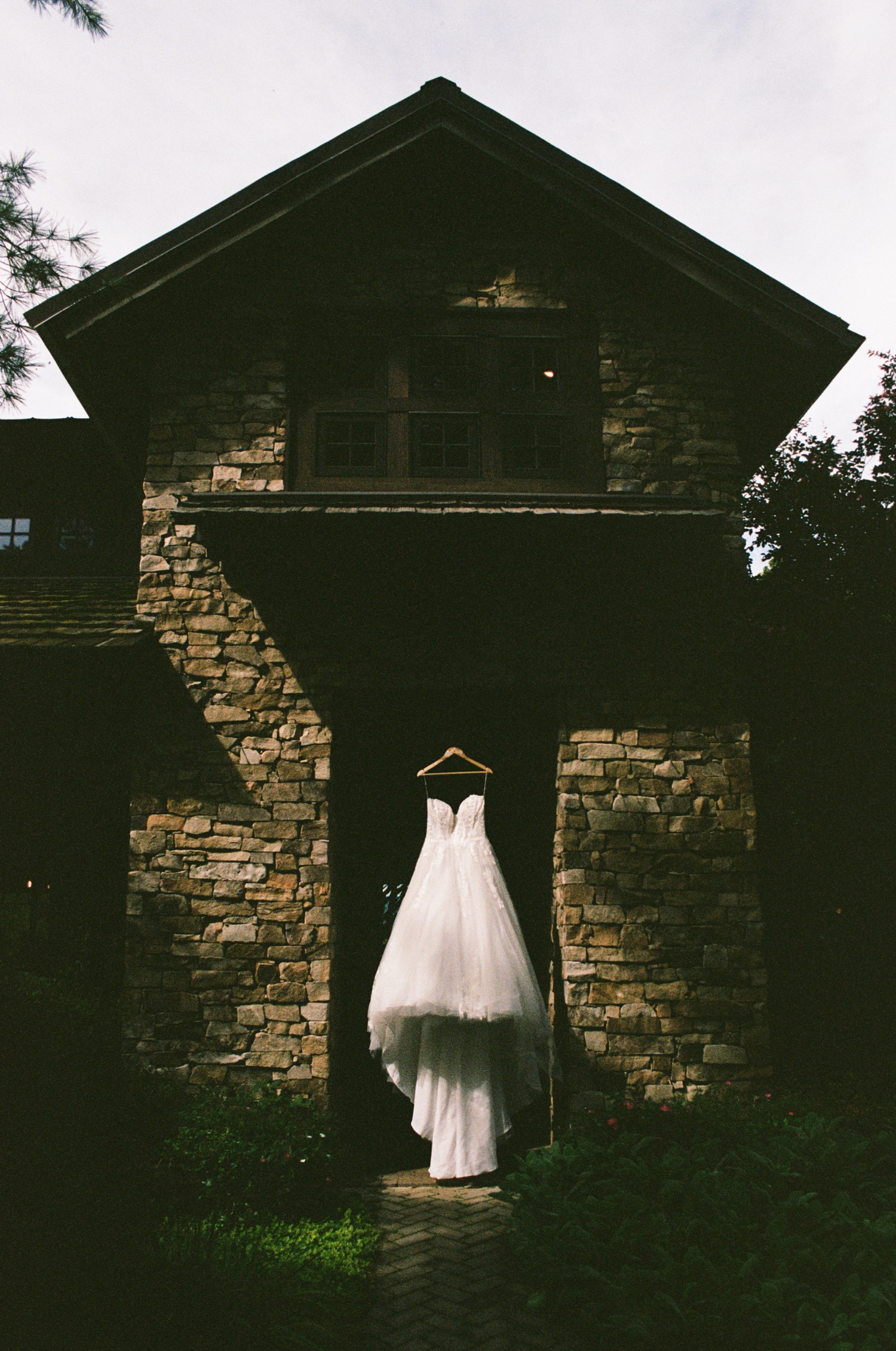 Photo by Laura Cate Photography pictures wedding dress hanging in front of old brick house.